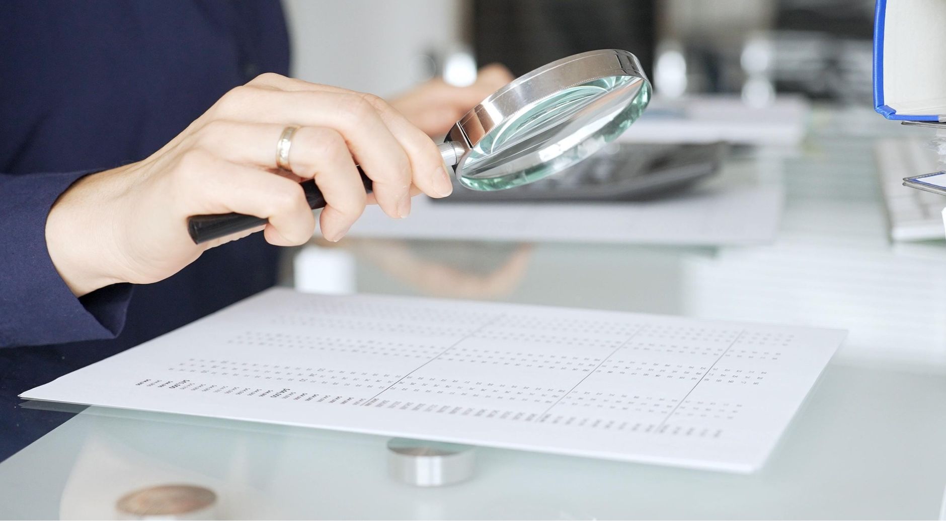 Compliance professional using a magnifying glass to review a death audit report.