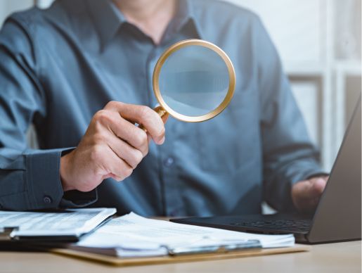 Magnifying glass held over paperwork during a mortality verification review.